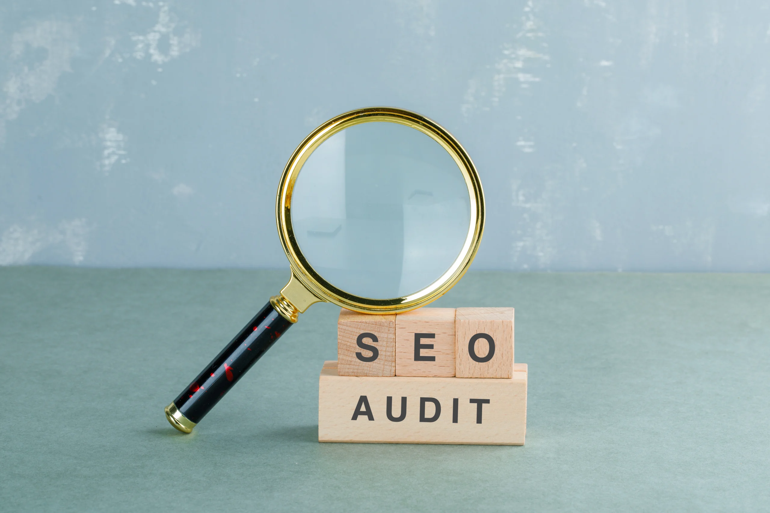 Audit SEO – Analyse et optimisation du site web Loupe au-dessus de blocs en bois avec inscription SEO Audit représentant l’analyse et l’audit SEO d’un site web